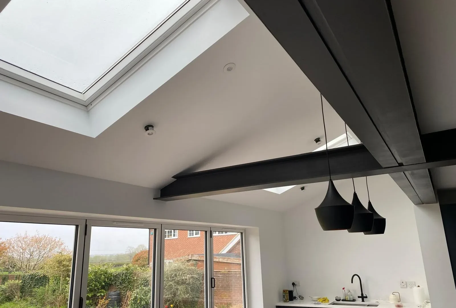 Finished kitchen extension with vaulted ceiling, dark exposed steel beams, skylights and bifold doors to the garden
