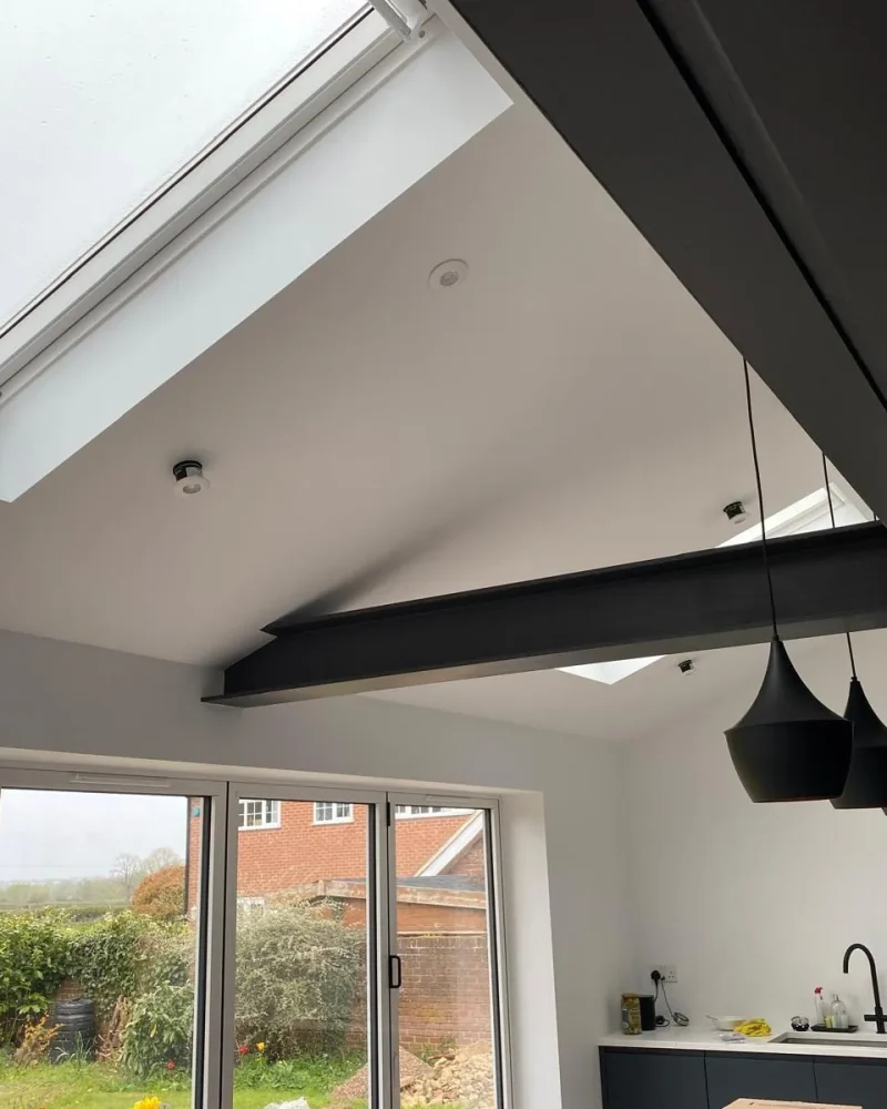 Finished kitchen extension with vaulted ceiling, dark exposed steel beams, skylights and bifold doors to the garden