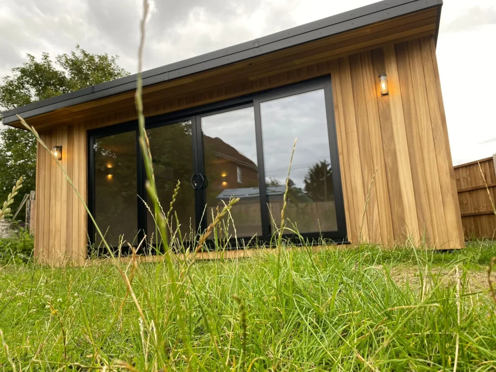 Low angle view of a timber-clad garden room with black-framed glazing seen across the lawn