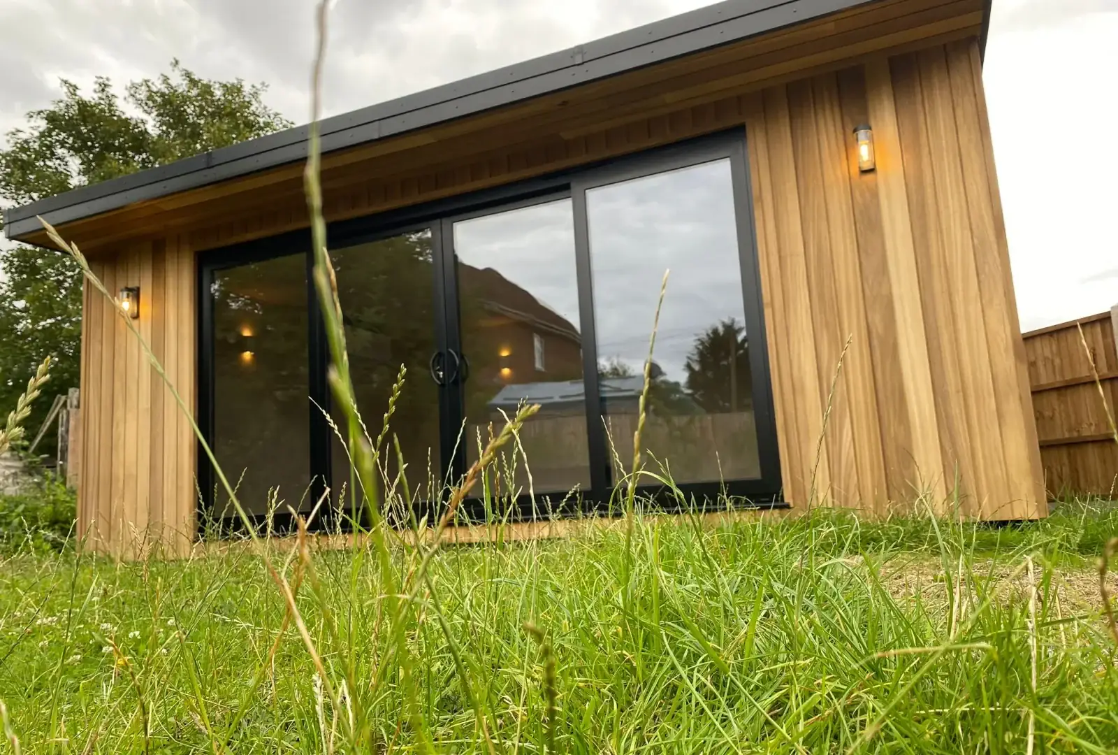 Low angle view of a timber-clad garden room with black-framed glazing seen across the lawn