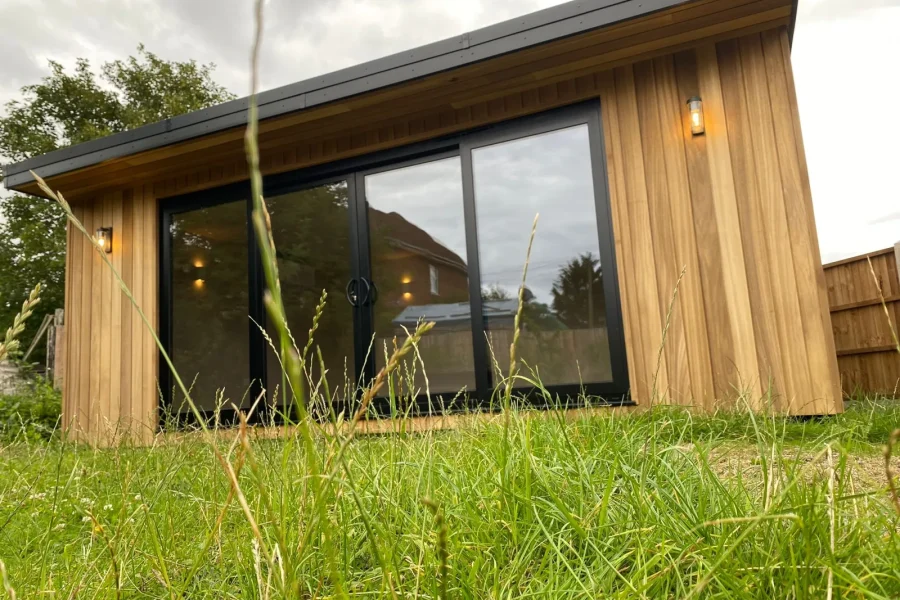 Low angle view of a timber-clad garden room with black-framed glazing seen across the lawn