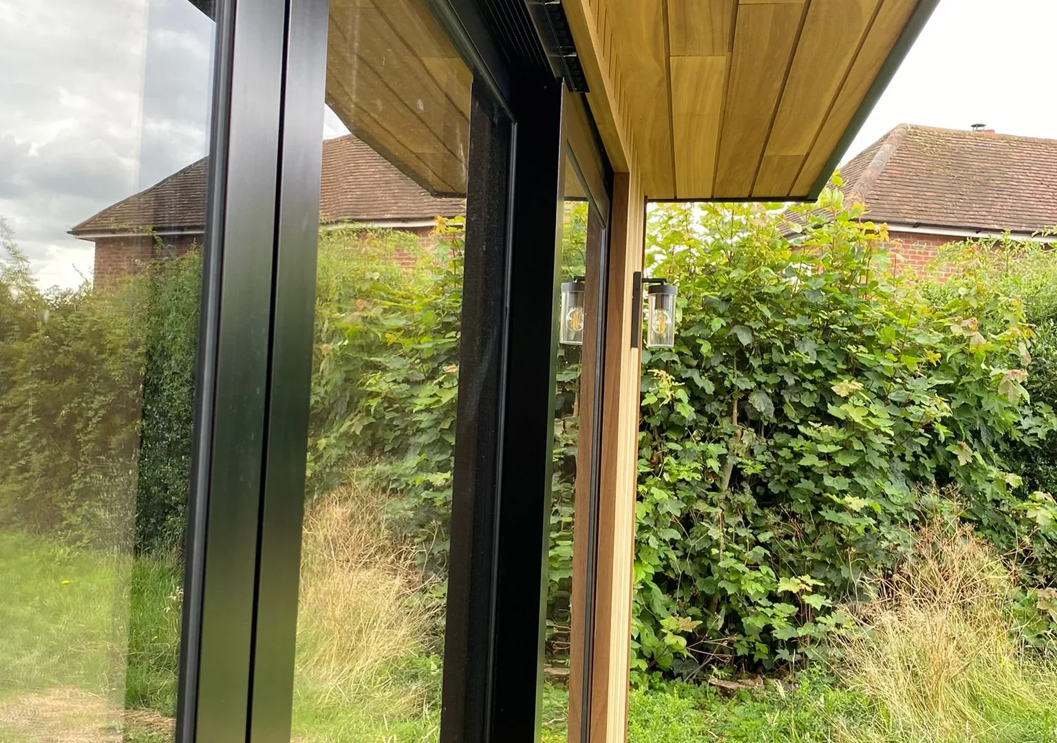 Close-up of the timber-clad soffit and black aluminium sliding door frames on a new garden room