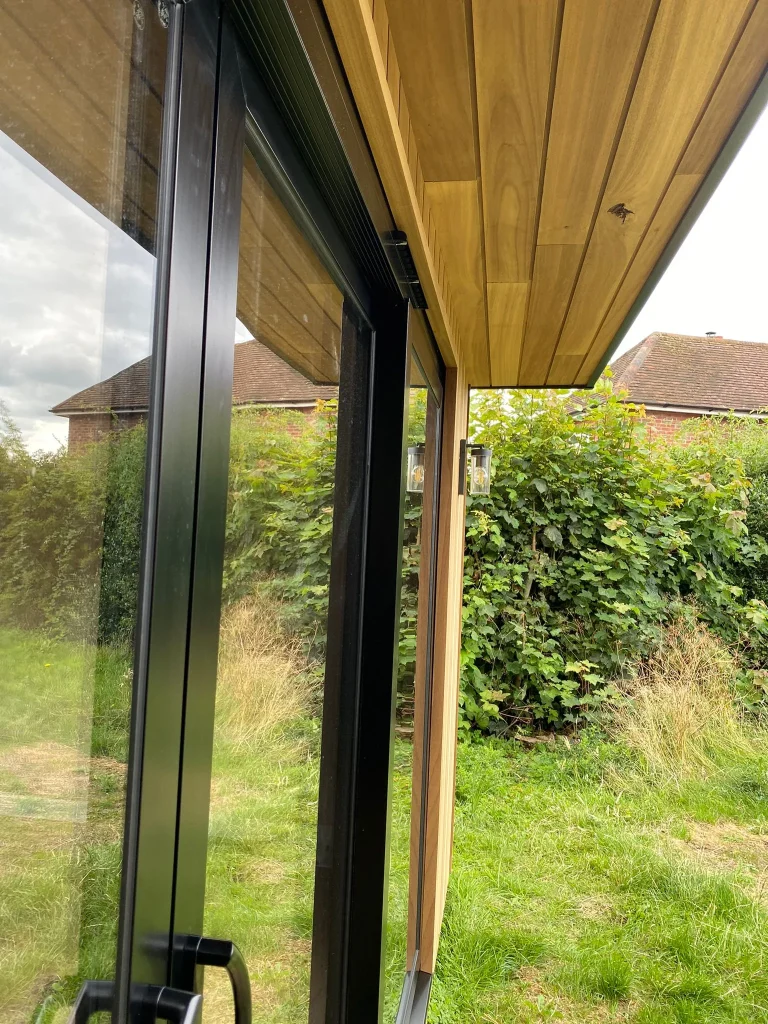 Close-up of the timber-clad soffit and black aluminium sliding door frames on a new garden room
