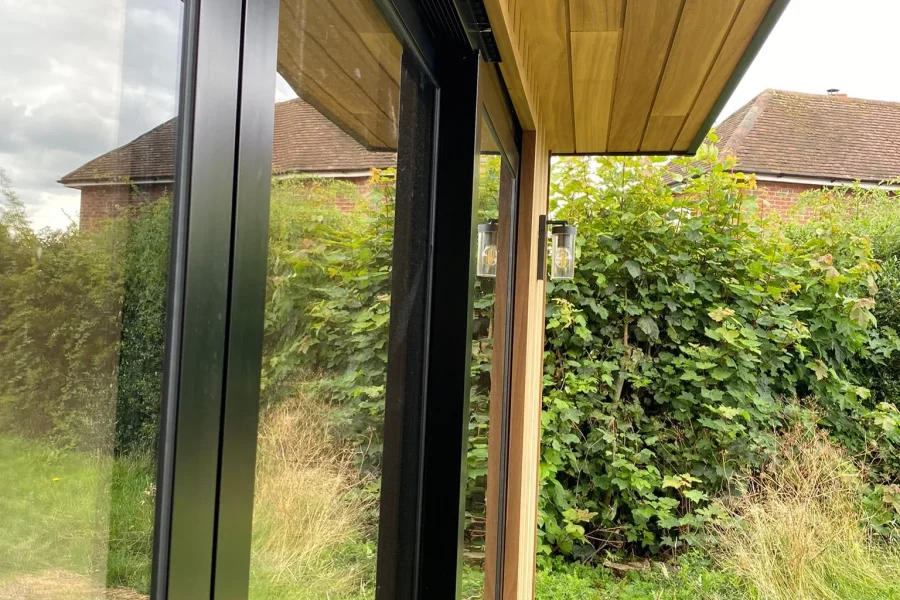 Close-up of the timber-clad soffit and black aluminium sliding door frames on a new garden room