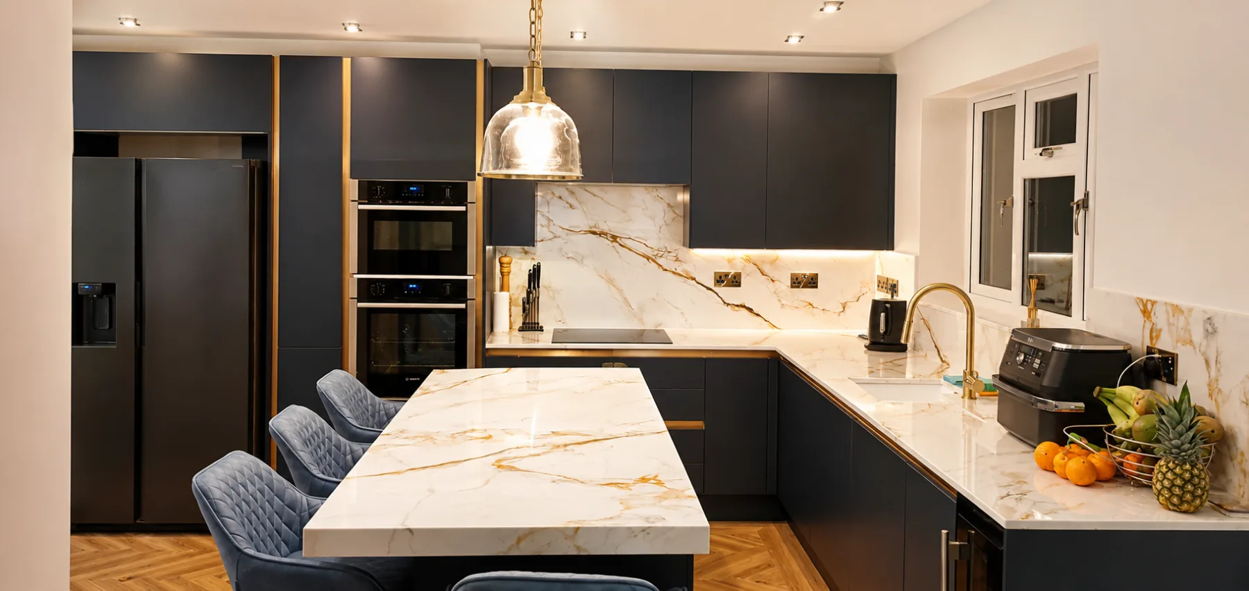 Handleless navy kitchen with marble effect quartz worktops and splashback, and integrated double ovens