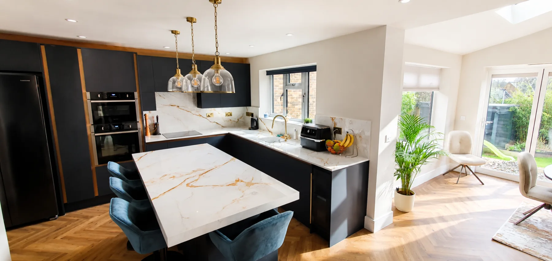 Open-plan kitchen extension with a marble effect island, brass pendant lights and herringbone flooring