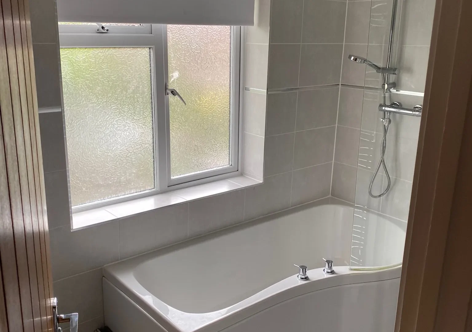 New bathroom with grey wall tiles, a P-shaped shower bath, glass screen, thermostatic shower and dark tiled floor