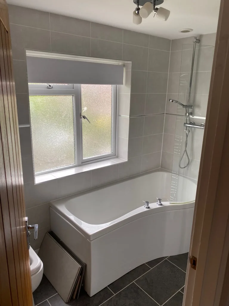 New bathroom with grey wall tiles, a P-shaped shower bath, glass screen, thermostatic shower and dark tiled floor