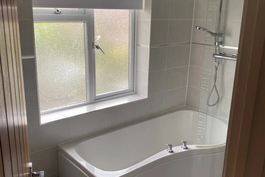 New bathroom with grey wall tiles, a P-shaped shower bath, glass screen, thermostatic shower and dark tiled floor