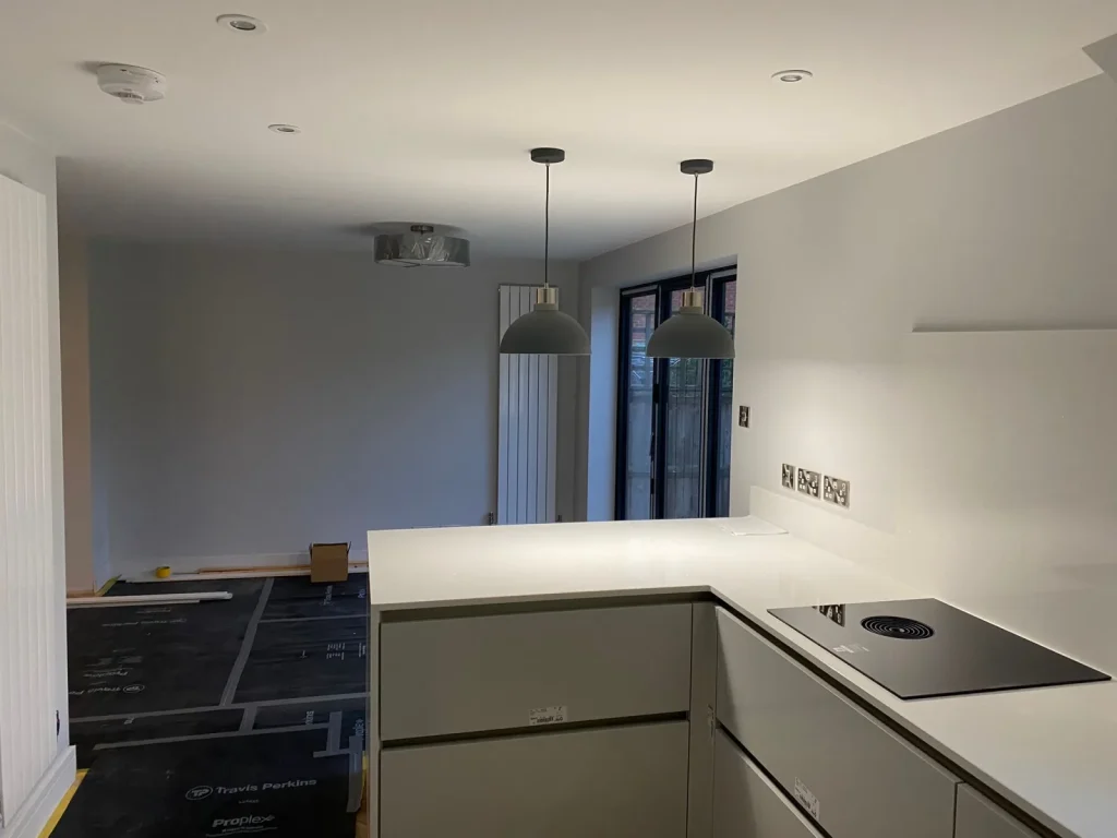 Kitchen with white quartz worktops, venting induction hob, pendant lights and dark-framed bifold doors during final fit-out