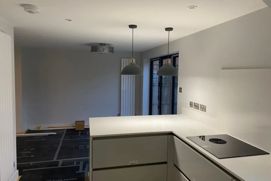 Kitchen with white quartz worktops, venting induction hob, pendant lights and dark-framed bifold doors during final fit-out