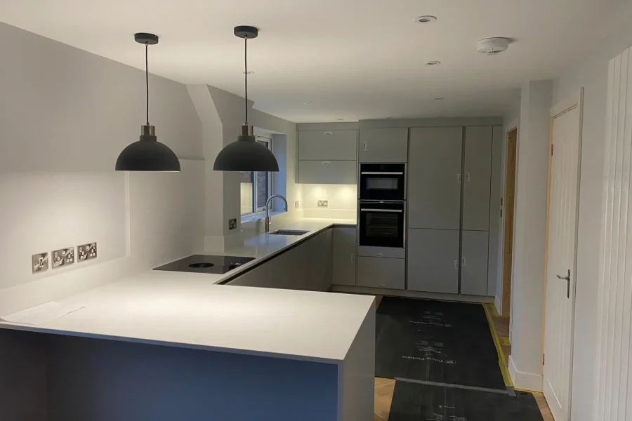 New grey handleless kitchen with white quartz worktops, a breakfast bar with pendant lights, induction hob and built-in ovens