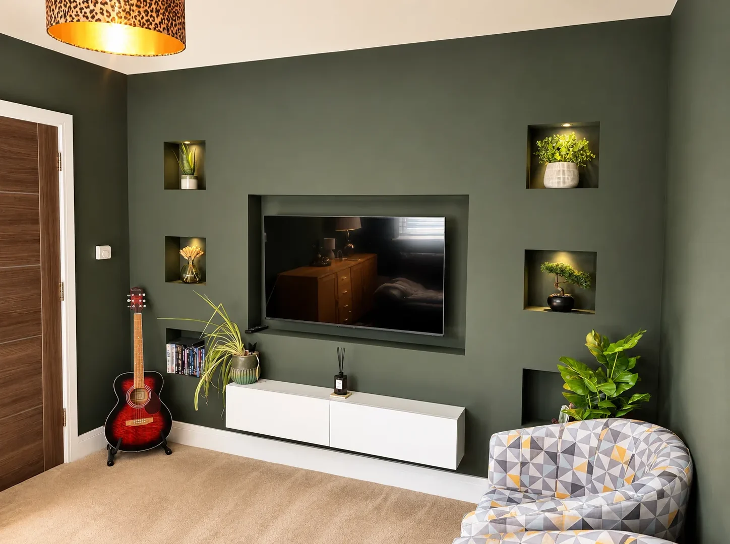 Dark green media wall with lit display alcoves, wall mounted TV and a floating white cabinet