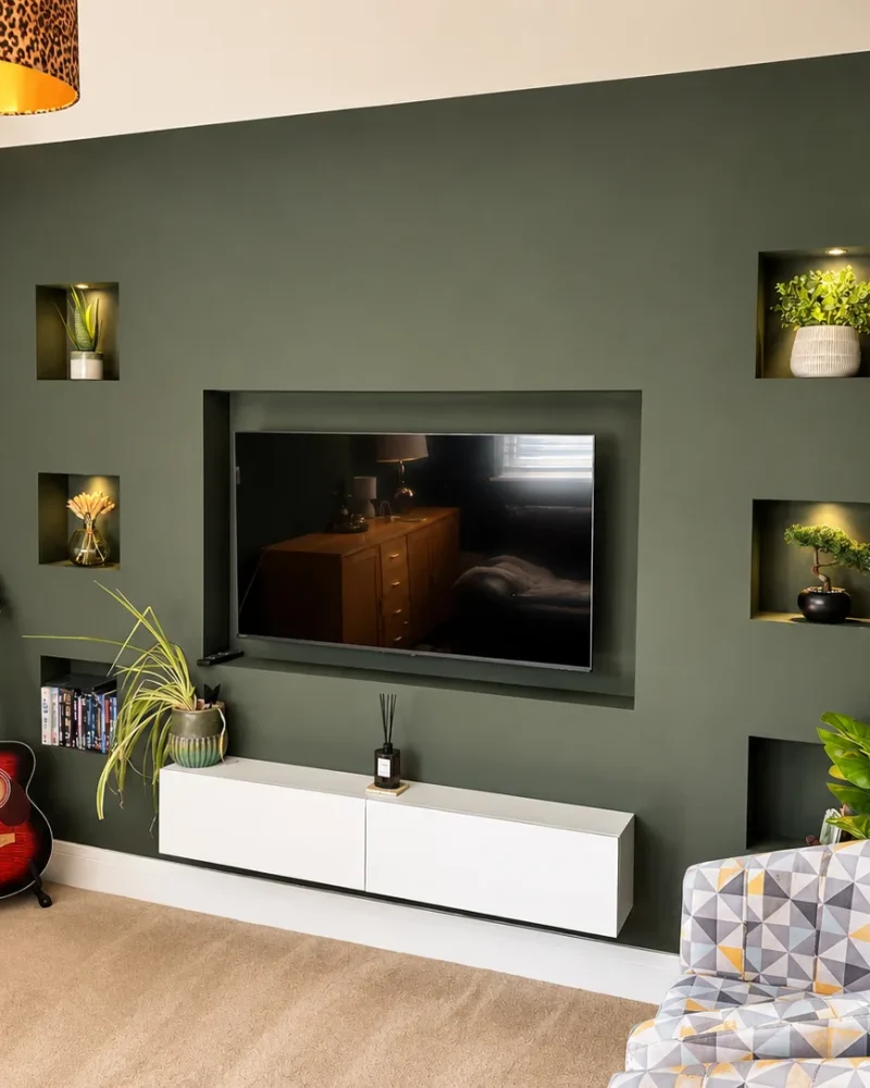 Dark green media wall with lit display alcoves, wall mounted TV and a floating white cabinet
