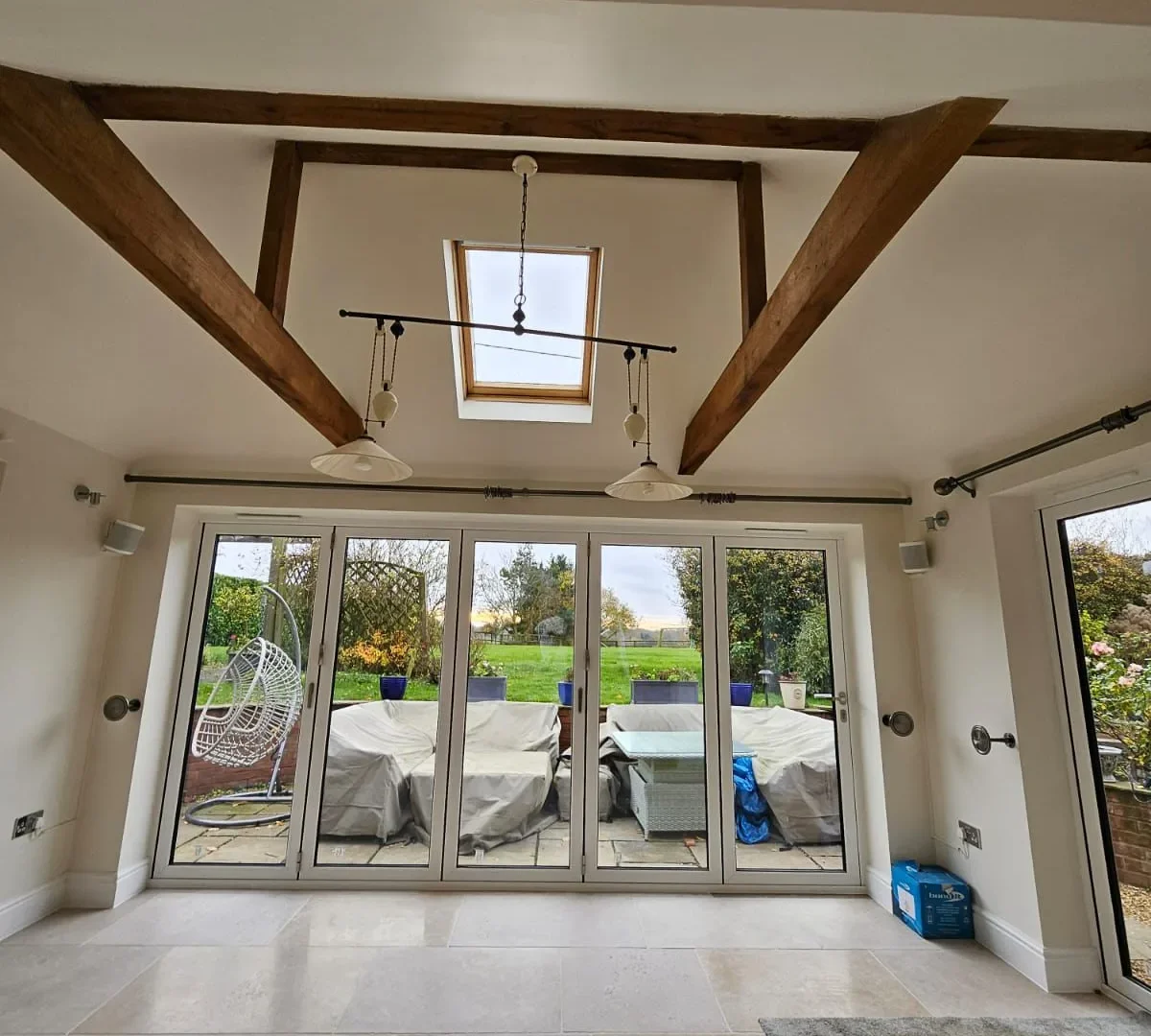 Vaulted room with exposed oak beams, a rooflight and white bifold doors opening onto the patio and garden