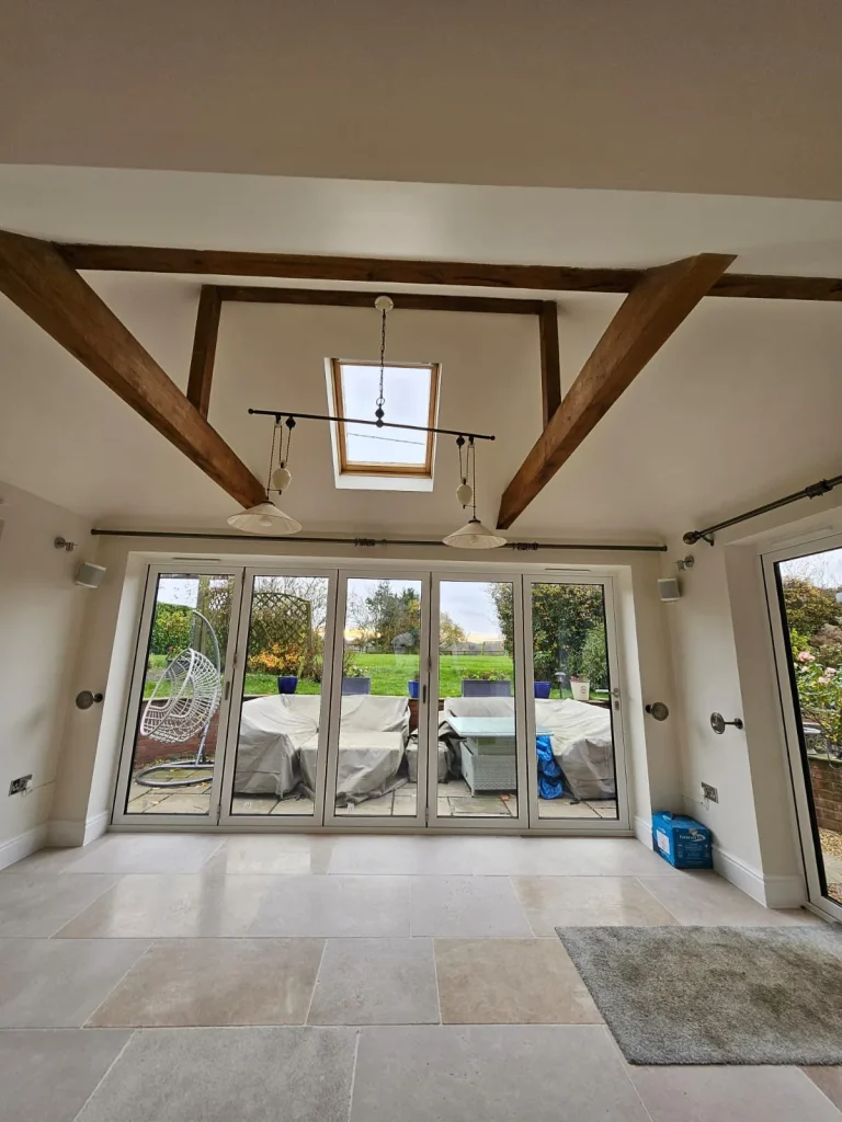 Vaulted room with exposed oak beams, a rooflight and white bifold doors opening onto the patio and garden