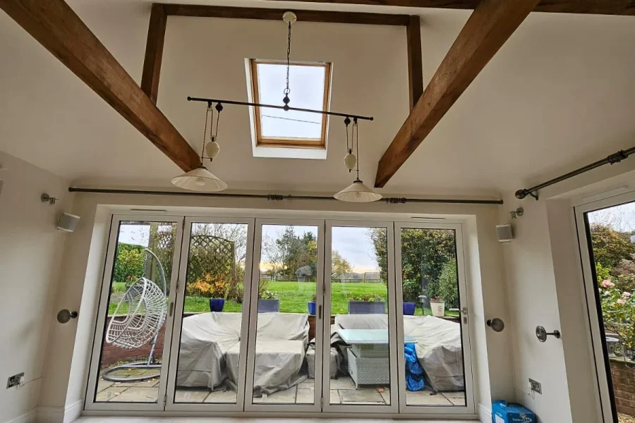 Vaulted room with exposed oak beams, a rooflight and white bifold doors opening onto the patio and garden