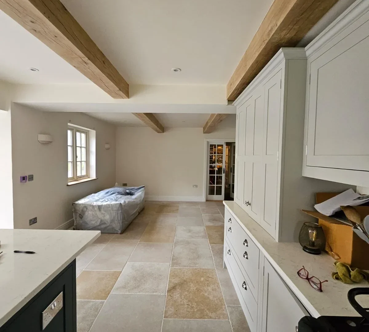 Renovated kitchen with exposed oak ceiling beams, pale shaker cabinetry, quartz worktops and limestone flagstone flooring