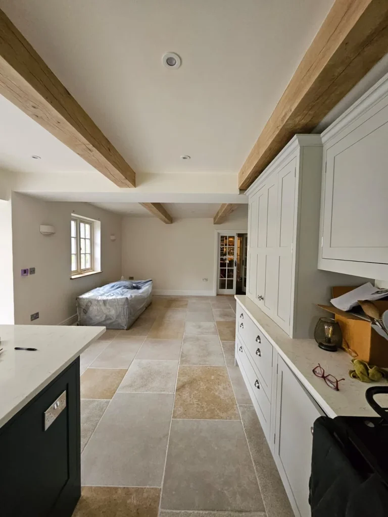 Renovated kitchen with exposed oak ceiling beams, pale shaker cabinetry, quartz worktops and limestone flagstone flooring