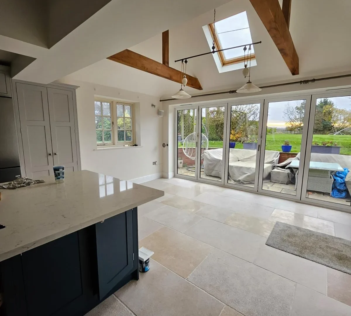 Open-plan kitchen with a navy island, quartz worktops, oak beams, rooflight and bifold doors to the garden