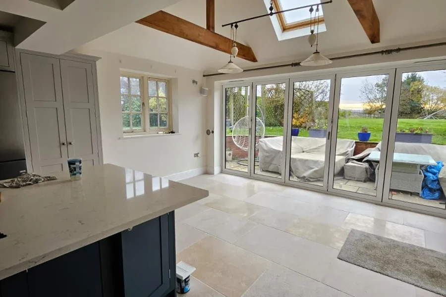 Open-plan kitchen with a navy island, quartz worktops, oak beams, rooflight and bifold doors to the garden