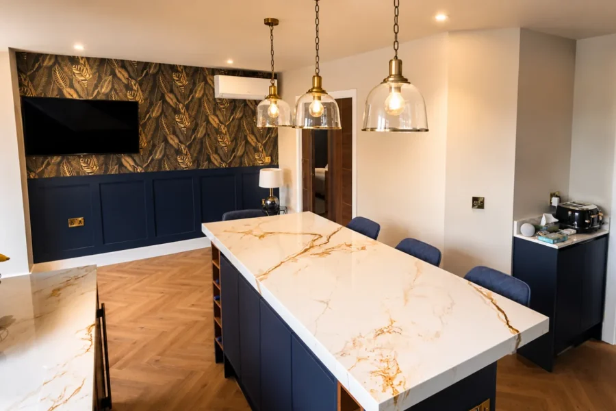 Navy kitchen island with a marble effect worktop, brass pendants and a panelled botanical feature wall