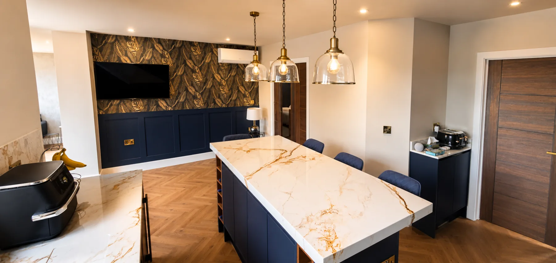 Navy kitchen island with a marble effect worktop, brass pendants and a panelled botanical feature wall