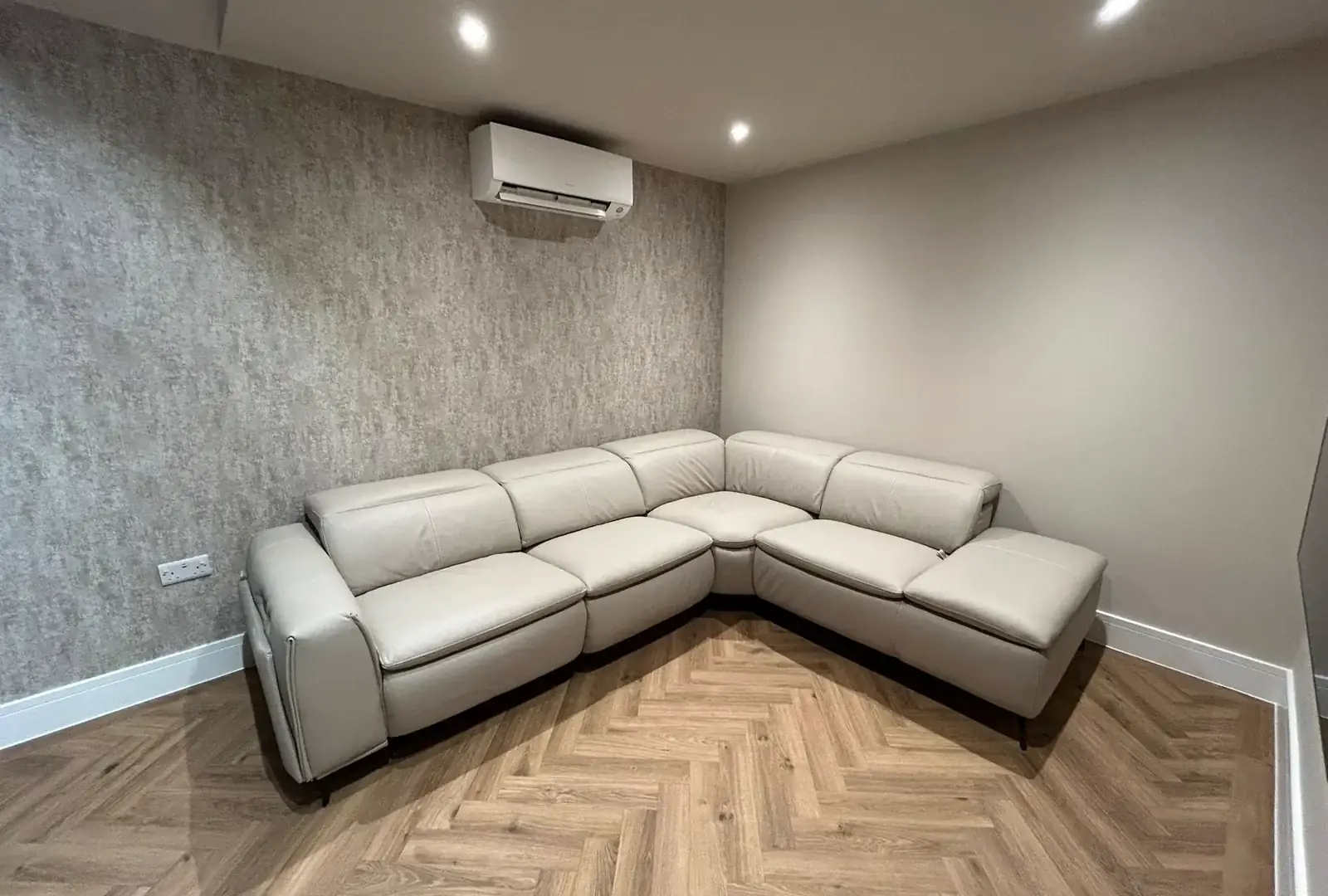 Finished media room with a grey leather corner sofa, herringbone flooring and soft ceiling lighting