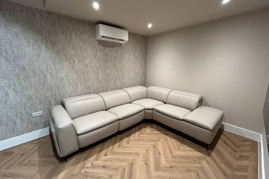 Finished media room with a grey leather corner sofa, herringbone flooring and soft ceiling lighting
